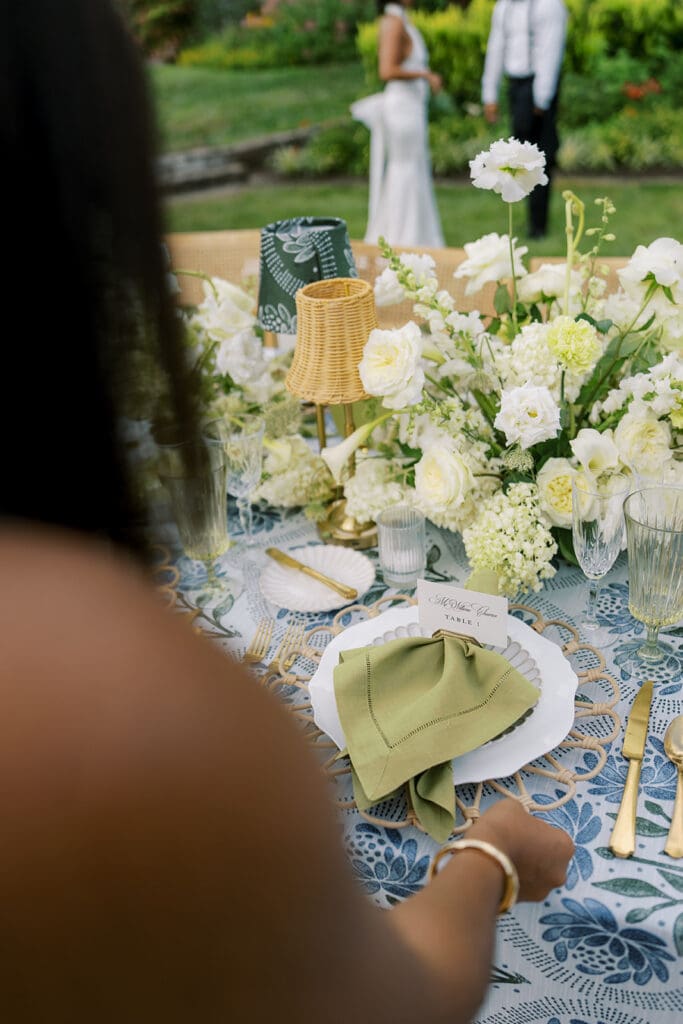 Wedding planner placing scalloped plate with rattan charger and sage napkin